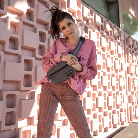 Woman outside on the sidewalk holding a Hex Instinct Grey Woven Waist Pack